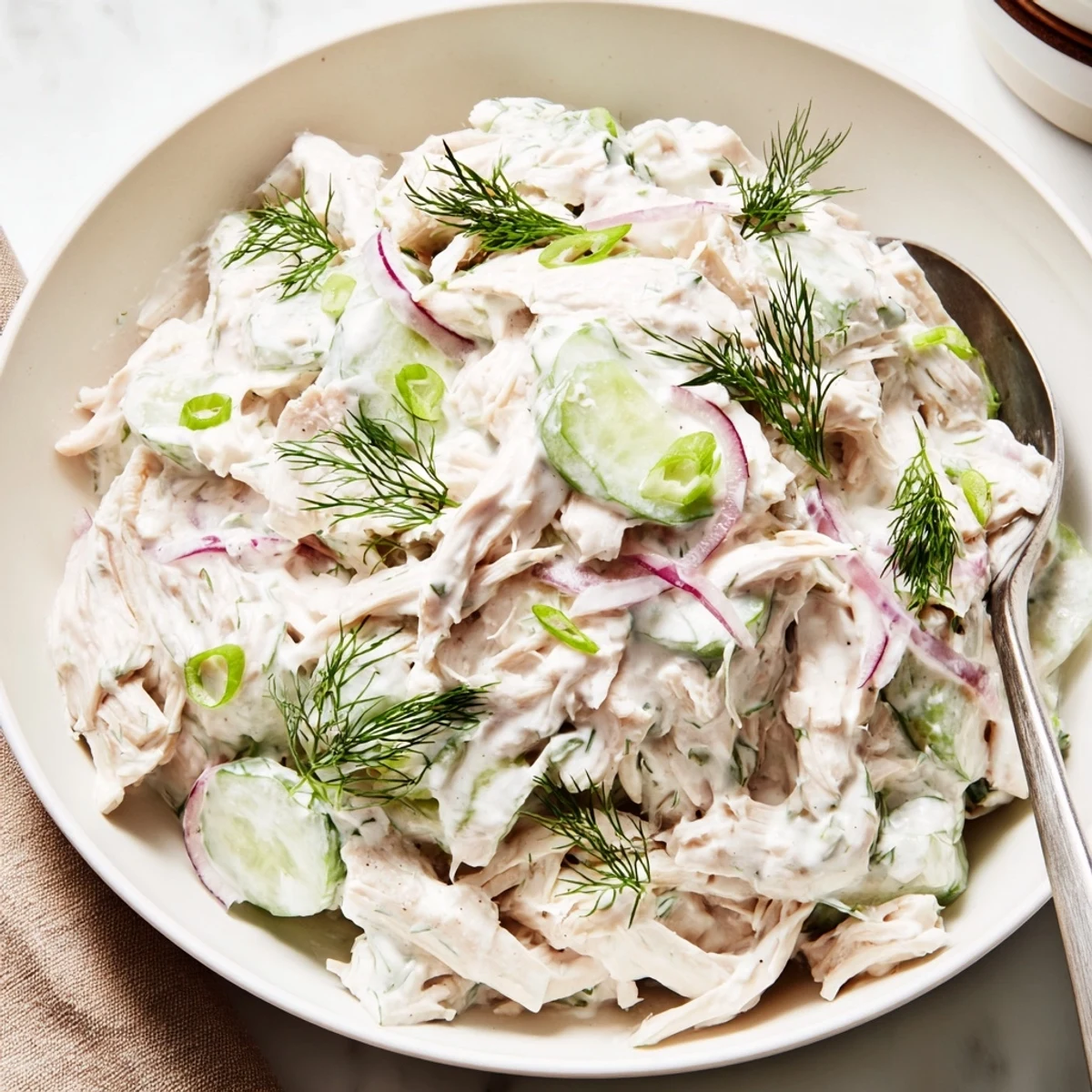 Serve Creamy Cucumber Chicken Salad in a white bowl, garnished with green onions and a lemon wedge for a refreshing light lunch.