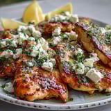 Juicy Greek Chicken with Lemon and Feta sizzling in a skillet topped with crumbled feta and parsley.