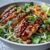 Brightly colored vegetables and sliced chicken over rice noodles in a serving bowl.