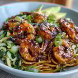 A close-up of Grilled Shrimp Asian Noodle Bowl featuring charred shrimp, crisp cucumber ribbons, fresh sprouts, and lime wedges.