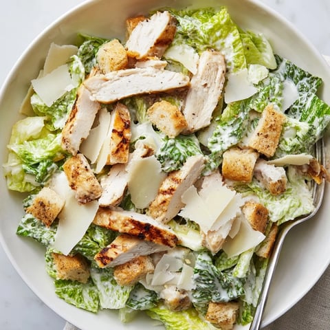 Freshly grilled chicken breast slices are fanned over crisp romaine lettuce tossed in creamy Caesar dressing, topped with crunchy croutons and shaved Parmesan for a classic Chicken Caesar Salad.