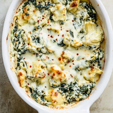 Freshly baked Spinach Artichoke Dip in a ceramic dish, bubbling with golden cheese and specks of green spinach, served with crispy toasted bread.