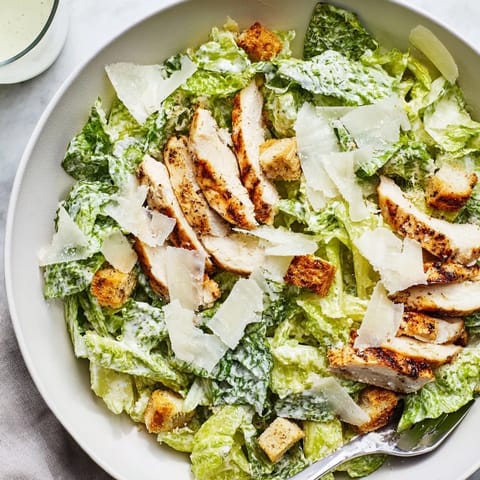 A close-up of the hearty Chicken Caesar Salad shows golden croutons and shaved Parmesan mingling with juicy grilled chicken on vibrant green romaine leaves.