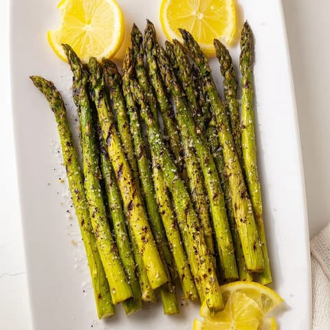 Perfectly charred Grilled Asparagus seasoned with sea salt and lemon wedges served alongside grilled chicken.