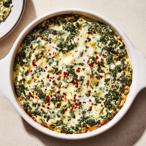 Creamy Spinach Artichoke Dip with a bubbly Parmesan crust, garnished with fresh spinach leaves and a side of crunchy tortilla chips for dipping.
