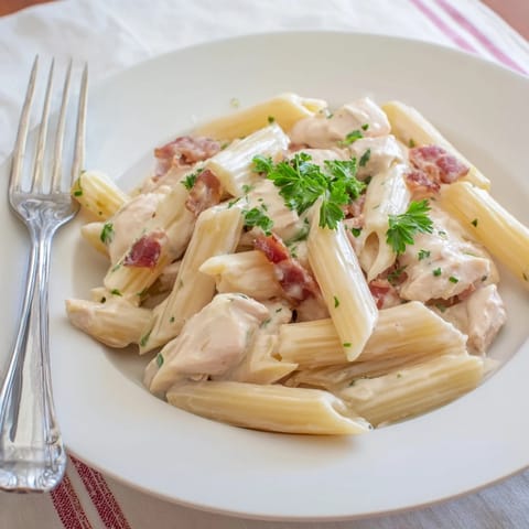 A close-up of Creamy Chicken Bacon Penne served in a white ceramic bowl with fresh parsley.  