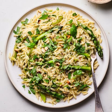 A vibrant bowl of Asparagus Lemon Orzo Salad features crisp greens, grated Parmesan, and a bright lemon-olive oil dressing, perfect for a light spring lunch.