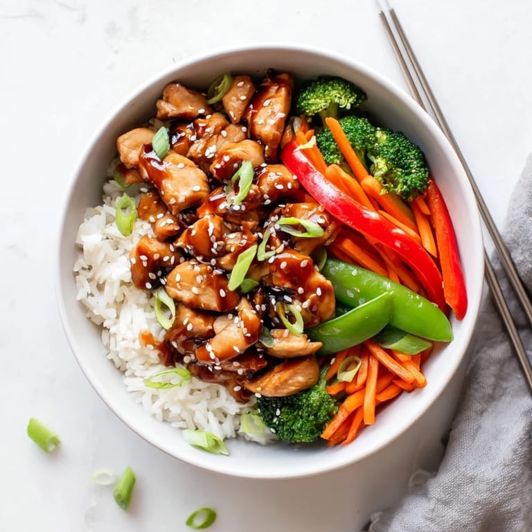 Close-up of tender teriyaki chicken topped with sesame seeds and sliced scallions, served over fluffy white rice.