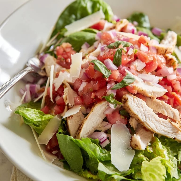 A vibrant Bruschetta Chicken Salad with grilled chicken slices, colorful tomato-basil topping, and mixed greens served with lemon wedges on a rustic platter.