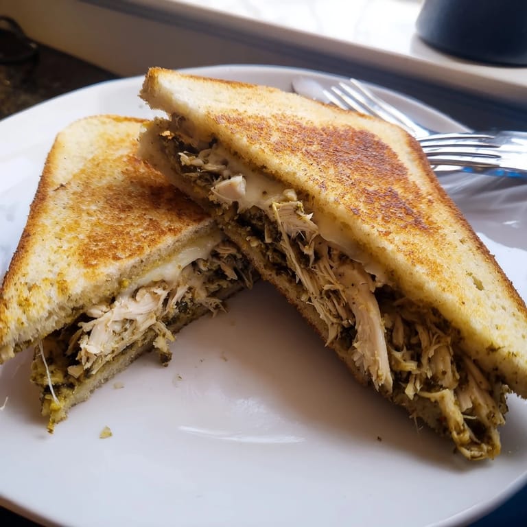 Freshly grilled bread slices cradle juicy chicken and mozzarella, with vibrant pesto peeking out from the warm, melted edges of this savory sandwich.