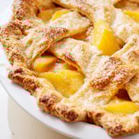 Golden-baked Peach Pie with a flaky crust, served warm with vanilla ice cream on a rustic table.