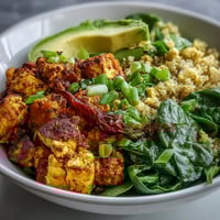 A vibrant bowl of Tofu Scramble Vegan Breakfast Bowl with golden tofu, roasted sweet potatoes, and creamy avocado slices for a nourishing start.  