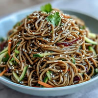 Cold soba noodle salad with sesame ginger dressing, featuring crisp julienned vegetables and a tangy, nutty sauce.